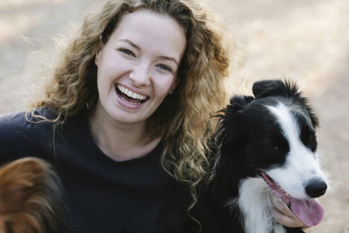 Young female owner with curly hair looking at camera and smiling while embracing obedient dogs in countryside