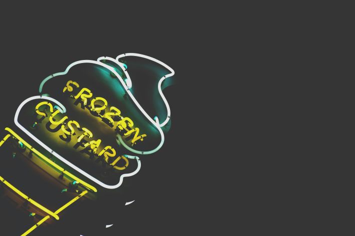 Vibrant neon frozen custard sign glowing against a dark background.