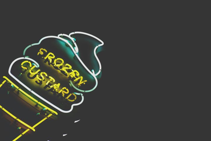 Vibrant neon frozen custard sign glowing against a dark background.