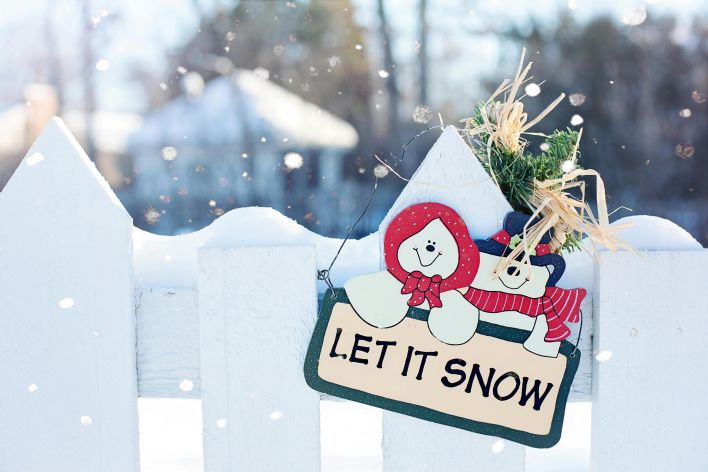 Festive winter scene with a whimsical 'Let It Snow' sign on a snowy fence.
