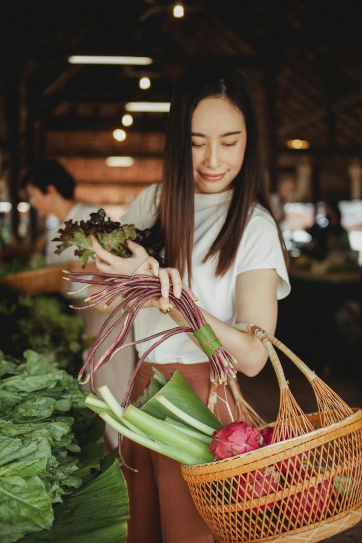 Woman selecting fresh produce at an indoor local market with a wicker basket.