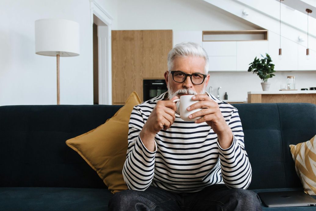 Senior man with glasses enjoying coffee in a modern living room.